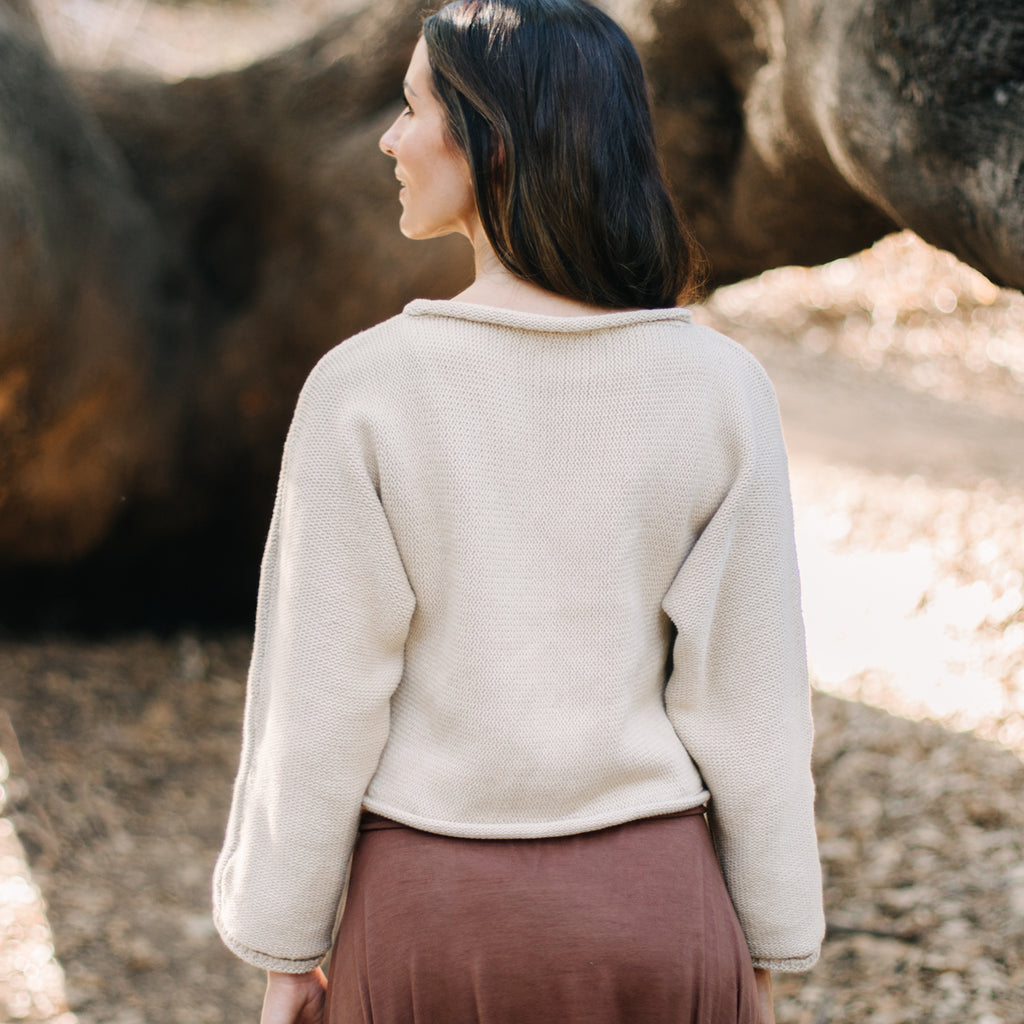 Woman standing in front of a tree, facing away. Wearing Sakti Rising Bagala Crop Sweater in Oat, sustainable and ethical yoga meditation apparel.