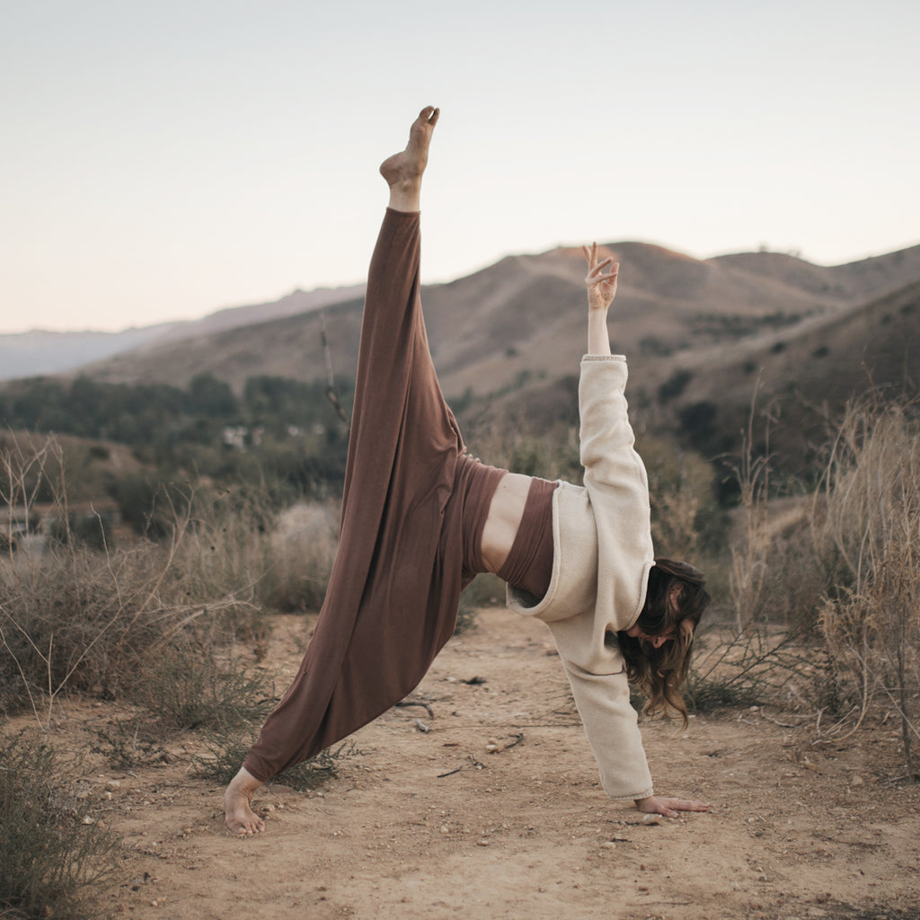 Woman practices yoga on mountaintop, wearing Sakti Rising Parvati Pants in Cacao. Ethical, Sustainable yoga apparel.