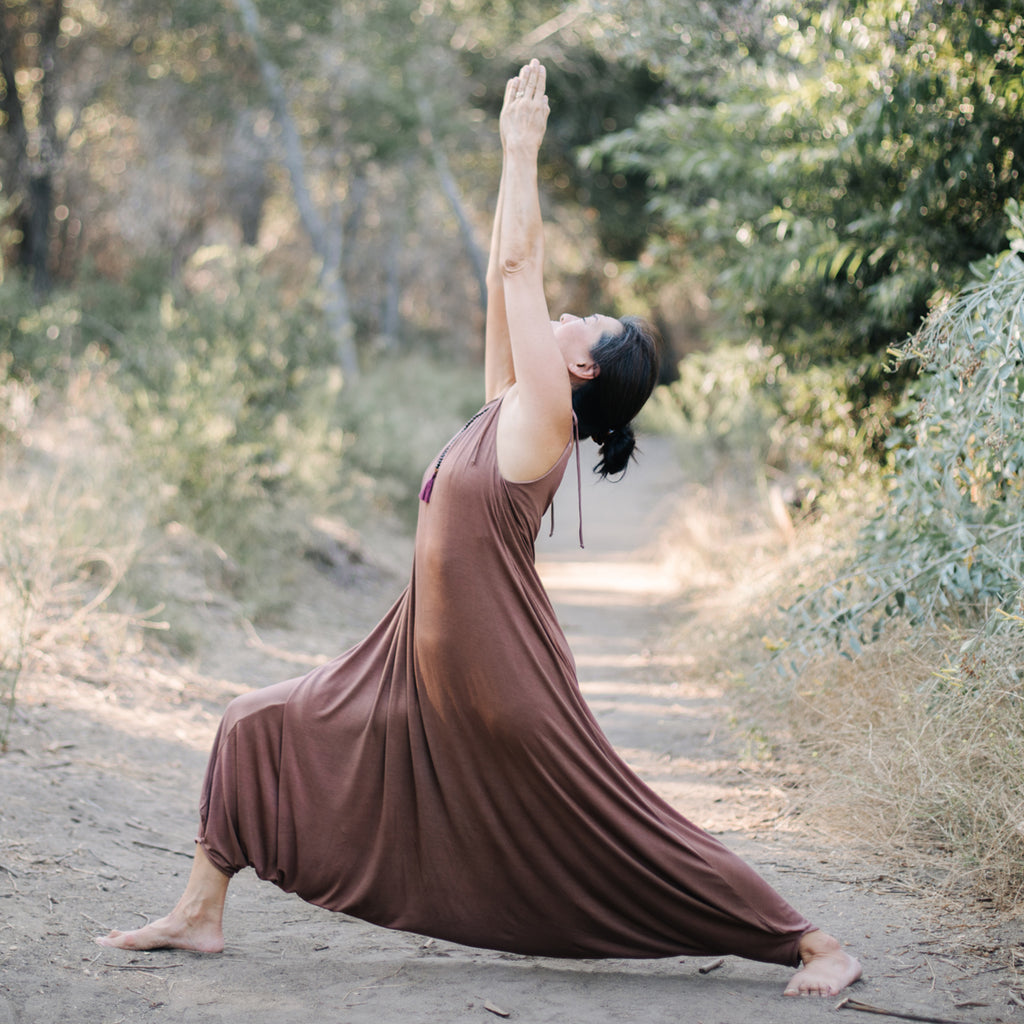 Asian woman practices yoga in forest, wearing Sakti Rising Parvati Playsuit in Cacao. Ethical sustainable yoga apparel. 