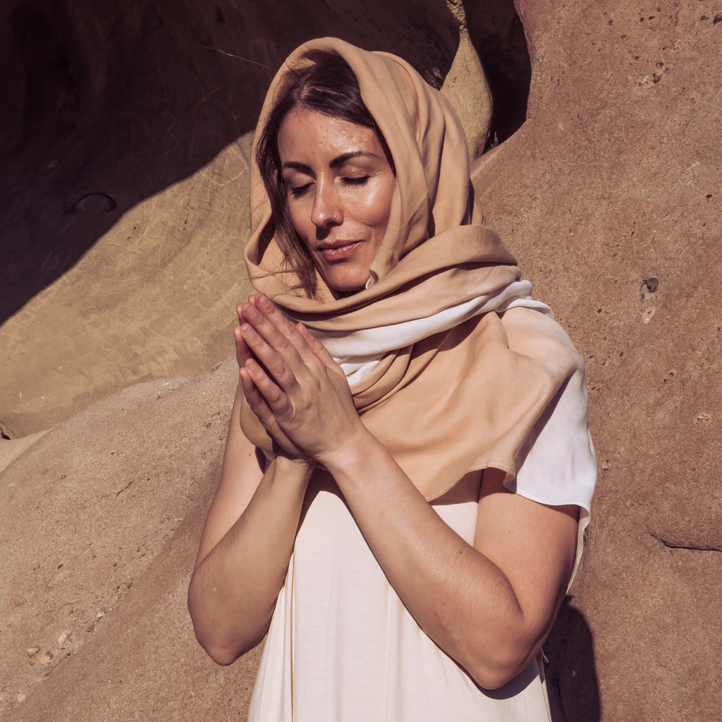 Image of a woman wrapped in Sakti Rising Buvaneshwari Shawl, eyes closed and hands in prayer. Ecofriendly sustainable yoga apparel that gives back to marginalized communities around the world.