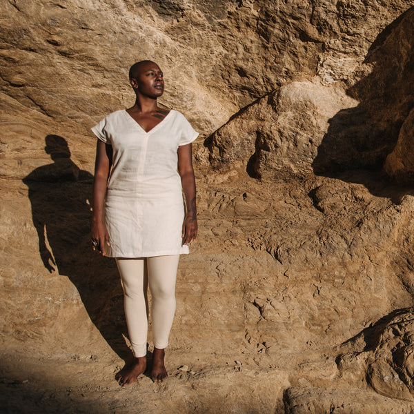 Black woman stands regally in front of sandstone cliff, wearing Sakti Rising Sita Tunic in Pearl. Ethical sustainable yoga apparel. 
