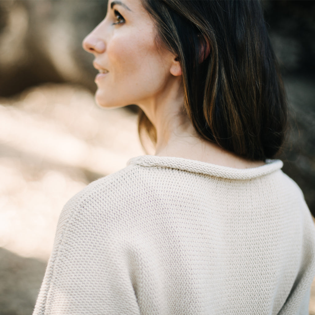 Back view of caucasian woman looking up and away.  Wearing Sakti Rising Bagala Crop Sweater in Oat, sustainable and ethical yoga meditation apparel.