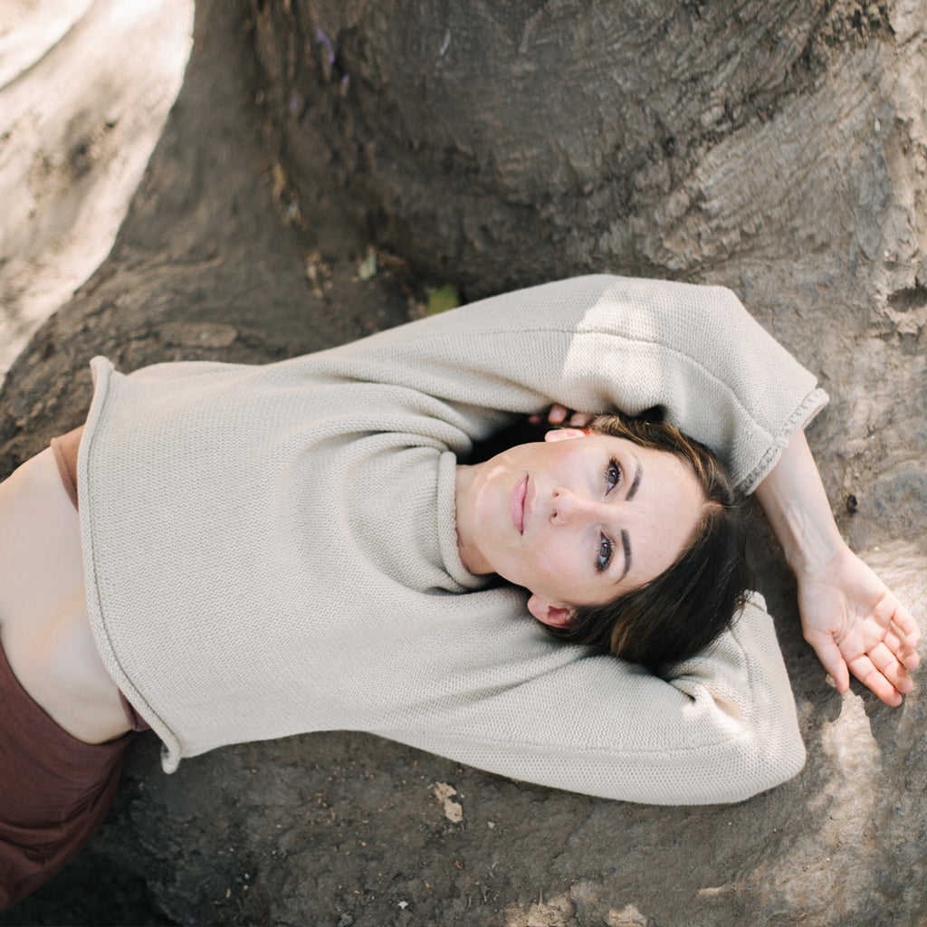 Caucasian woman lounging in tree. Wearing Sakti Rising Bagala Crop Sweater in Oat, sustainable and ethical yoga meditation apparel
