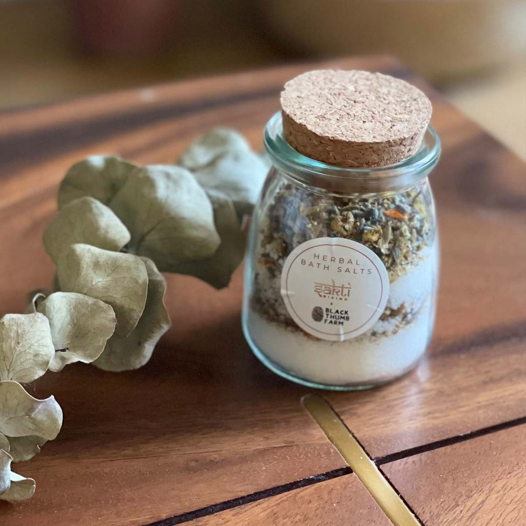 Sakti Rising and Black Thumb Farm herbal bath salts. Sustainably and ethically sourced. Small glass jar with cork lid, containing herbal bath salt blend.