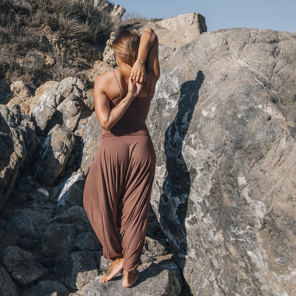 Woman on rocks practicing yoga, wearing Sakti Rising Parvati Pants in Cacao. Ethical, Sustainable yoga apparel.