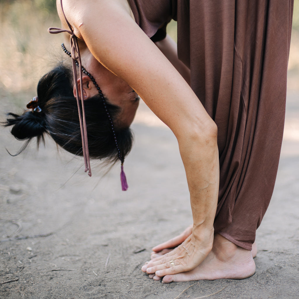 Asian woman bows to ground, wearing Sakti Rising Parvati Playsuit in Cacao. Ethical sustainable yoga apparel. 