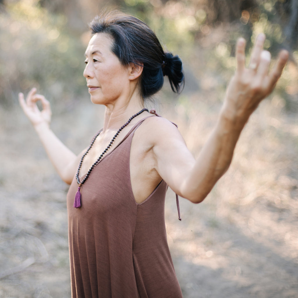 Asian woman with hands in mudra, wearing Sakti Rising Parvati Playsuit in Cacao. Ethical sustainable yoga apparel. 