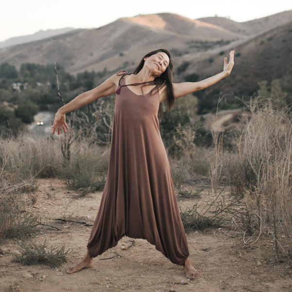 Asian woman dances on mountaintop, wearing Sakti Rising Parvati Playsuit in Cacao. Ethical sustainable yoga apparel. 