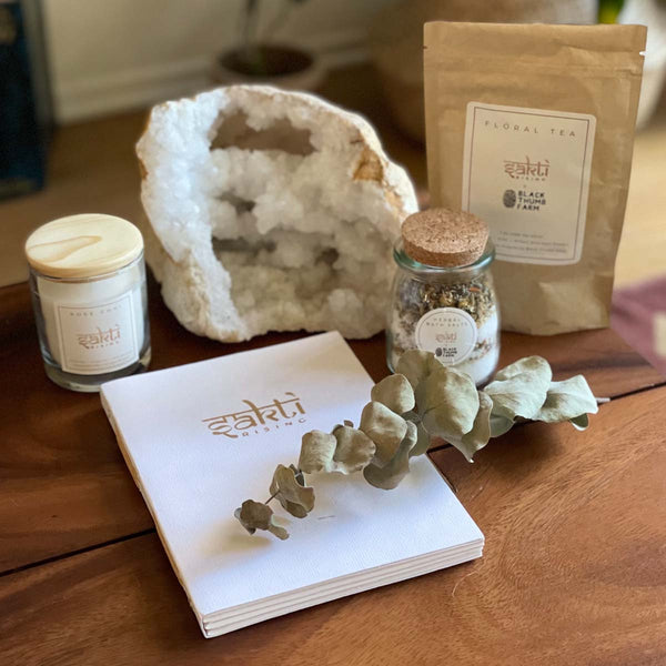 Sakti Rising Self Love Bundle: Sustainable and ethically sourced journal, candle, bath salts, and herbal tea shown with a calming crystal
