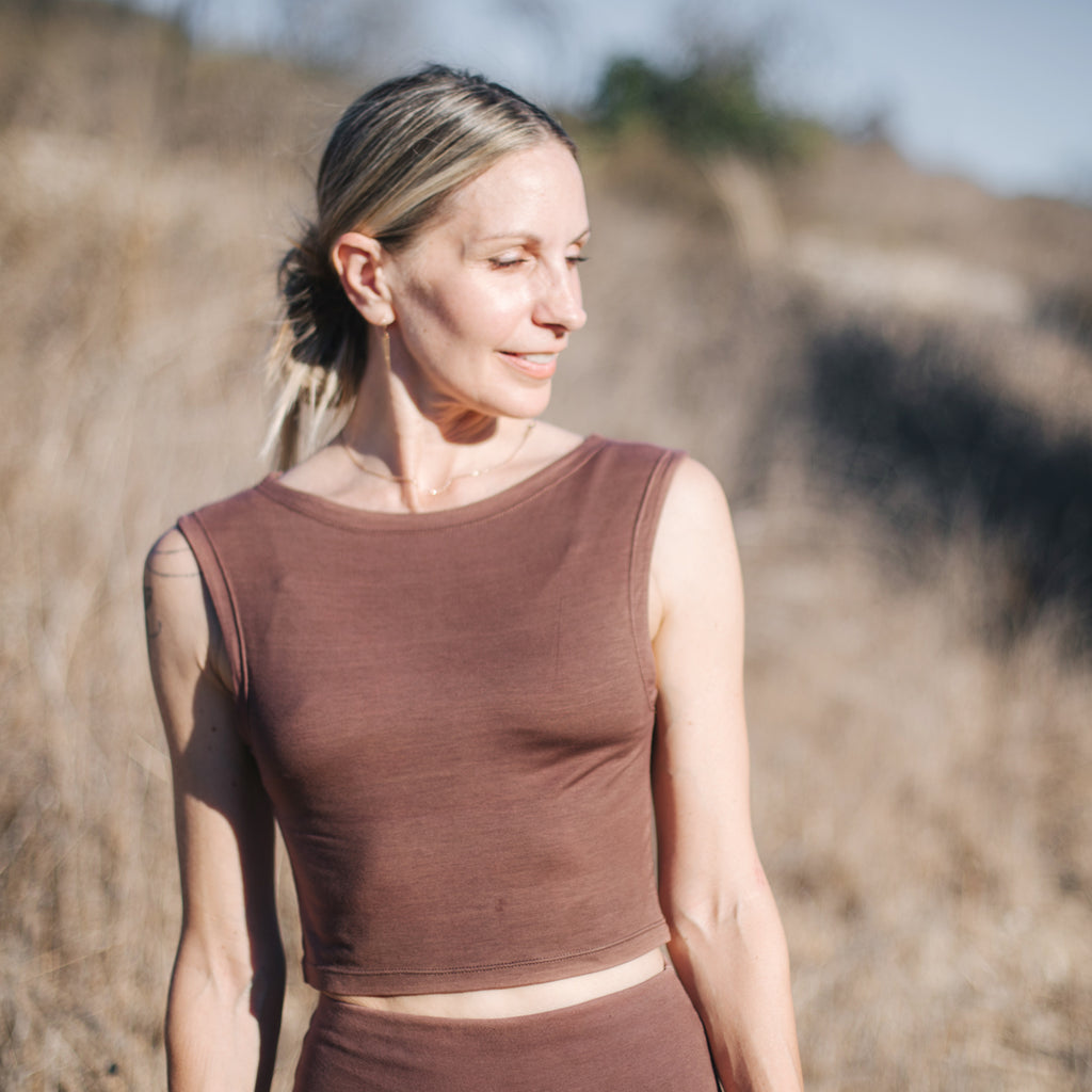 Caucasian woman smiles in field, wearing Sakti Rising Tara Tank in Cacao. Ethical, sustainable yoga apparel.