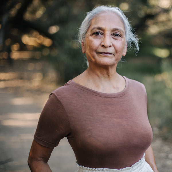 Portrait of elderly Indian woman wearing Sakti Rising Tara Tee in Cacao. Ethical sustainable yoga apparel. 